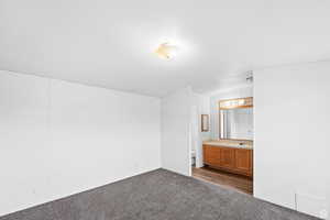 Unfurnished bedroom with dark carpet, lofted ceiling, and ensuite bathroom