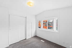 Unfurnished bedroom with carpet, a closet, and lofted ceiling