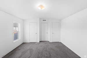 Unfurnished bedroom featuring carpet, vaulted ceiling, and two closets