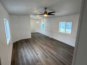 Empty room with dark wood-type flooring, ceiling fan, and hanging lights