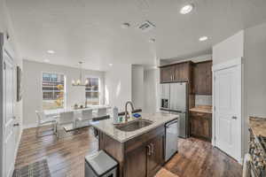 Kitchen featuring dark brown cabinets, light stone counters, appliances with stainless steel finishes, recessed lighting, and pendant lighting