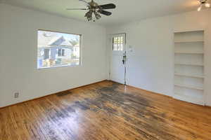 Empty room with wood-type flooring, plenty of natural light, built in features, and ceiling fan