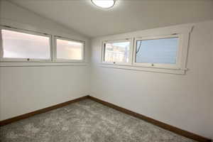 Carpeted empty room featuring lofted ceiling and baseboards