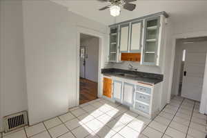 Kitchen with dark countertops, light tile patterned flooring, glass insert cabinets, and ceiling fan