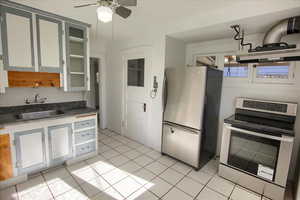 Kitchen featuring appliances with stainless steel finishes, light tile patterned floors, dark countertops, and under cabinet range hood