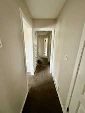 Corridor featuring dark colored carpet and baseboards