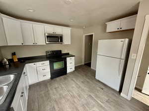 Kitchen featuring black electric range oven, freestanding refrigerator, white cabinets, stainless steel microwave, and dark countertops