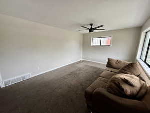 Carpeted living area featuring a ceiling fan and baseboards