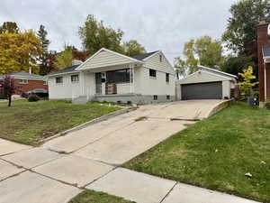 View of front of house with a front yard, an outbuilding, brick siding, a detached garage, and covered porch