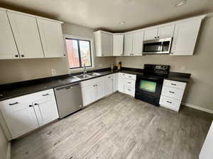 Kitchen featuring stainless steel appliances, white cabinets, dark countertops, light wood-style floors, and recessed lighting