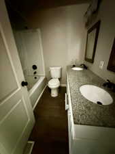 Bathroom with dark wood-type flooring, double vanity, and bathtub / shower combination