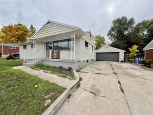 Bungalow-style house featuring a detached garage, an outdoor structure, a front yard, and brick siding