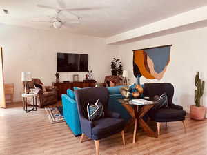 Living room with a textured wall, light wood finished floors, and a ceiling fan