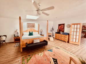 Bedroom featuring a skylight, light wood-type flooring, a ceiling fan, and a textured wall