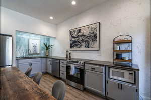 Kitchen featuring a textured wall, gray cabinetry, appliances with stainless steel finishes, light wood finished floors, and recessed lighting