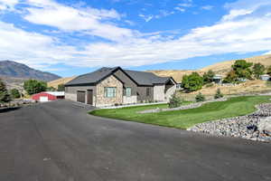 View of front of house with stone siding, a mountain view, a garage, a front lawn, and driveway