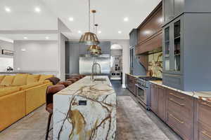 Kitchen with a waterfall island, quartize countertops, premium appliances, glass insert cabinets, and tasteful backsplash