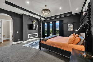Master Bedroom featuring a raised ceiling, a glass covered fireplace, recessed lighting, arched walkways, and a chandelier