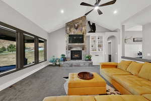 Carpeted living room featuring high vaulted ceiling, a fireplace, built in features, arched walkways, and ceiling fan