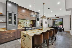 Kitchen featuring glass insert cabinets, tasteful backsplash, light stone countertops, a kitchen breakfast bar, and recessed lighting