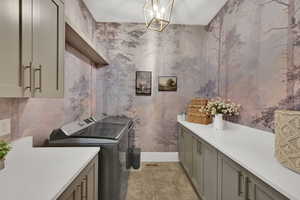 Washroom featuring wallpapered walls, washer and dryer, and a chandelier