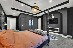 Bedroom featuring a tray ceiling, arched walkways, carpet, a glass covered fireplace, and recessed lighting