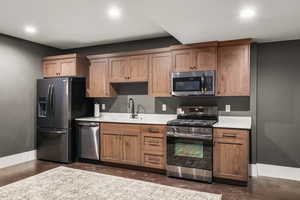 Kitchen with appliances with stainless steel finishes, light stone countertops, brown cabinets, and recessed lighting