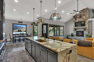 Kitchen with decorative light fixtures, high vaulted ceiling, light stone countertops, open floor plan, and a kitchen island with sink