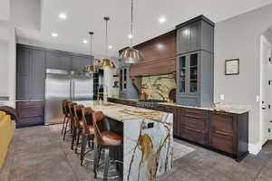 Kitchen with a breakfast bar, light stone counters, stainless steel appliances, pendant lighting, and a spacious island