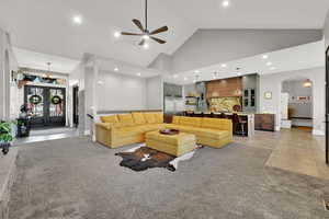 Living area with arched walkways, high vaulted ceiling, french doors, a chandelier, and light colored carpet