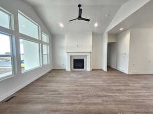 Unfurnished living room featuring ceiling fan, recessed lighting, wood finished floors, a tiled fireplace, and high vaulted ceiling
