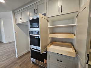 Kitchen with gray cabinetry, dark wood finished floors, stainless steel microwave, and light countertops