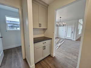 Kitchen with a chandelier, dark wood-style flooring, decorative light fixtures, tasteful backsplash, and dark stone countertops