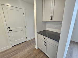 Bar with dark wood-style floors, tasteful backsplash, and white cabinets