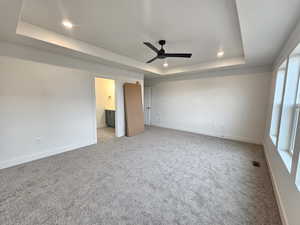 Unfurnished bedroom with a raised ceiling, ensuite bath, light colored carpet, a ceiling fan, and recessed lighting