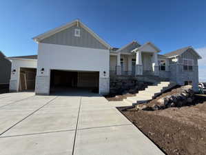 Craftsman house with board and batten siding, concrete driveway, stone siding, an attached garage, and a porch
