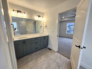 Ensuite bathroom with double vanity, light carpet, a textured ceiling, and ceiling fan