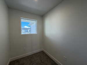 Spare room featuring dark colored carpet and baseboards