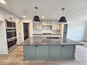 Kitchen with backsplash, stainless steel appliances, dark stone countertops, decorative light fixtures, and a center island with sink