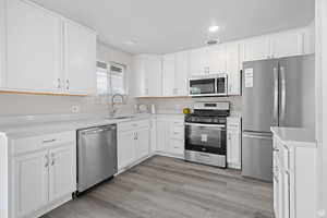 Kitchen with stainless steel appliances, light wood-type flooring, white cabinetry, and recessed lighting