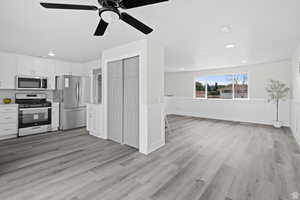 Kitchen featuring white cabinetry, stainless steel appliances, light countertops, a wainscoted wall, and light wood finished floors