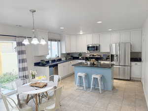 Kitchen with appliances with stainless steel finishes, pendant lighting, a kitchen island, a kitchen bar, and a chandelier