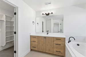 Full bath featuring vanity, light tile patterned floors, a garden tub, and a spacious closet