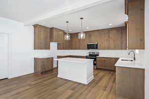 Kitchen with hanging light fixtures, stainless steel appliances, brown cabinetry, a center island, and dark wood finished floors