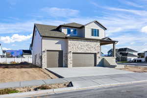 View of front of home with driveway, stone siding, a garage, a mountain view, and a porch