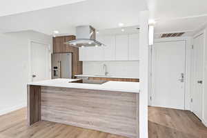 Kitchen featuring modern cabinets, island range hood, high end refrigerator, white cabinets, and light wood-style floors