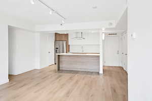 Kitchen with modern cabinets, light countertops, light wood-style flooring, wall chimney exhaust hood, and brown cabinetry