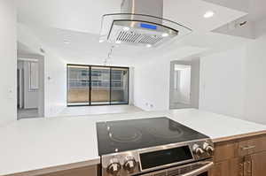 Kitchen featuring electric range, island range hood, recessed lighting, open floor plan, and brown cabinetry