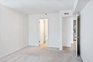 Bedroom with light colored carpet, high quality fridge, and connected bathroom