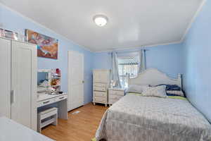 Bedroom featuring light wood-style flooring, ornamental molding, and vaulted ceiling
